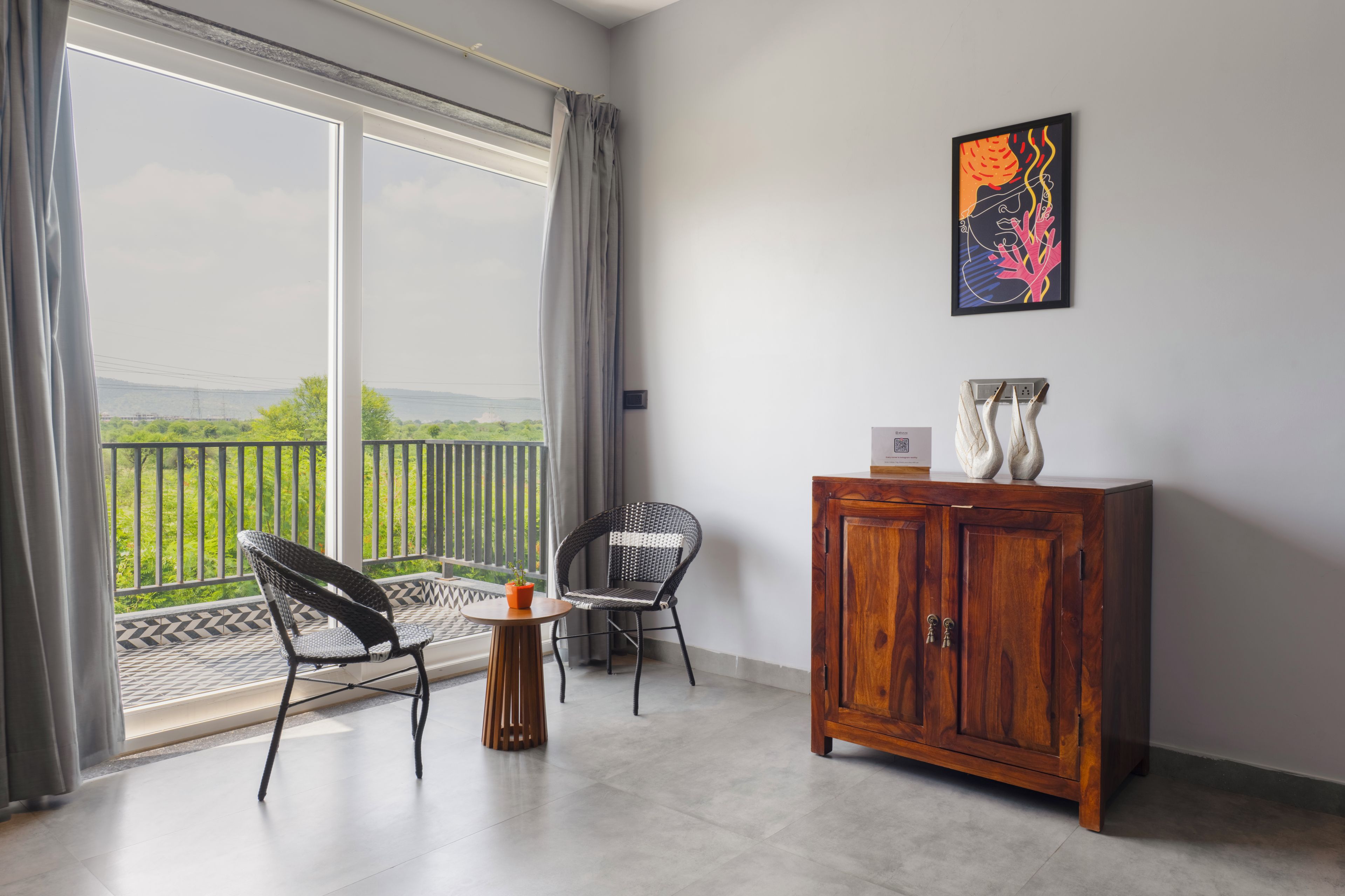 A room with a balcony, two wicker chairs, a small wooden table, and a cabinet.