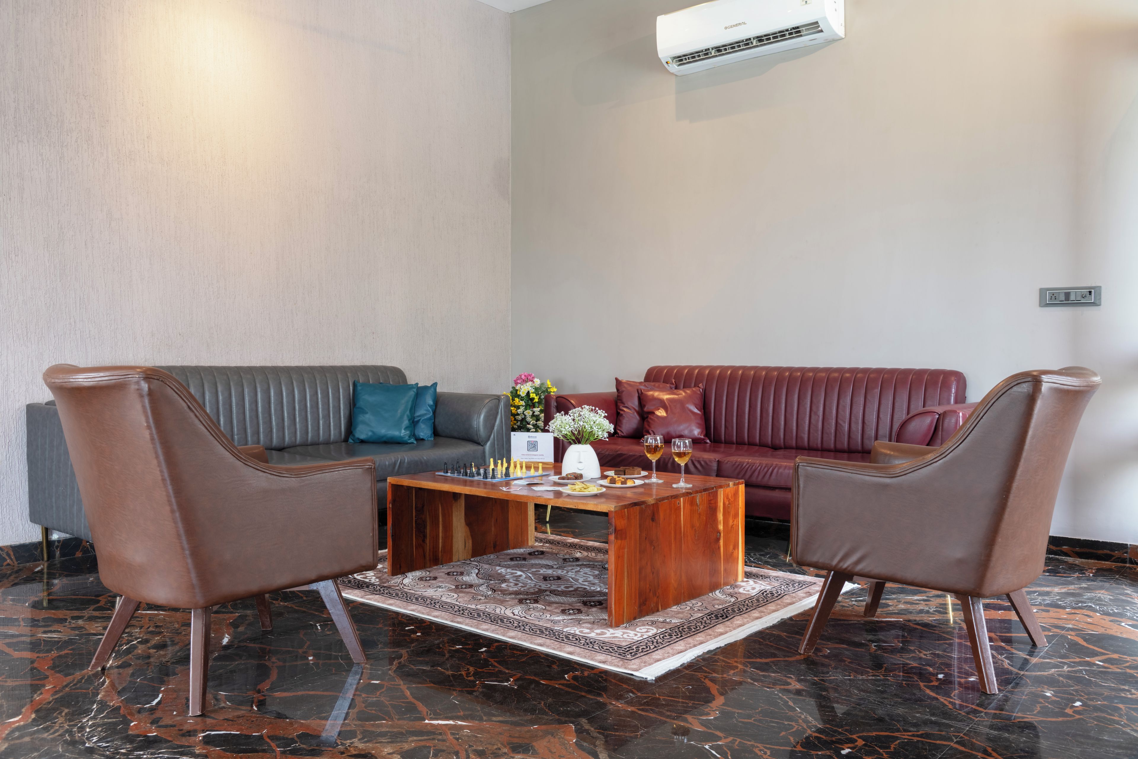 Una sala moderna con un sofá gris, un sofá rojo y dos sillones marrones. Hay una mesa de centro con un juego de ajedrez y un jarrón de flores.