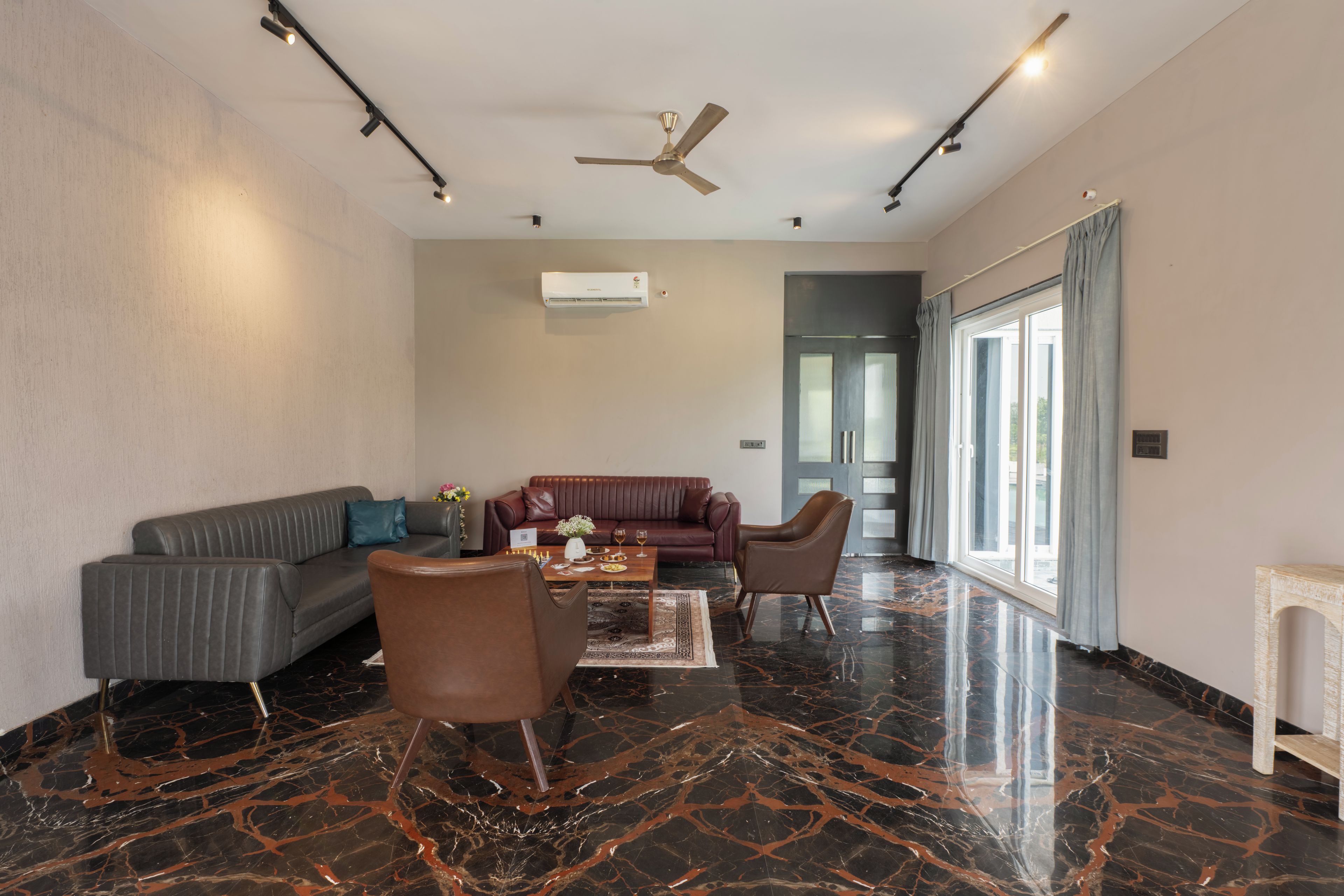 Una sala moderna con un sofá gris, un sillón de cuero marrón, una mesa de centro y un ventilador de techo.