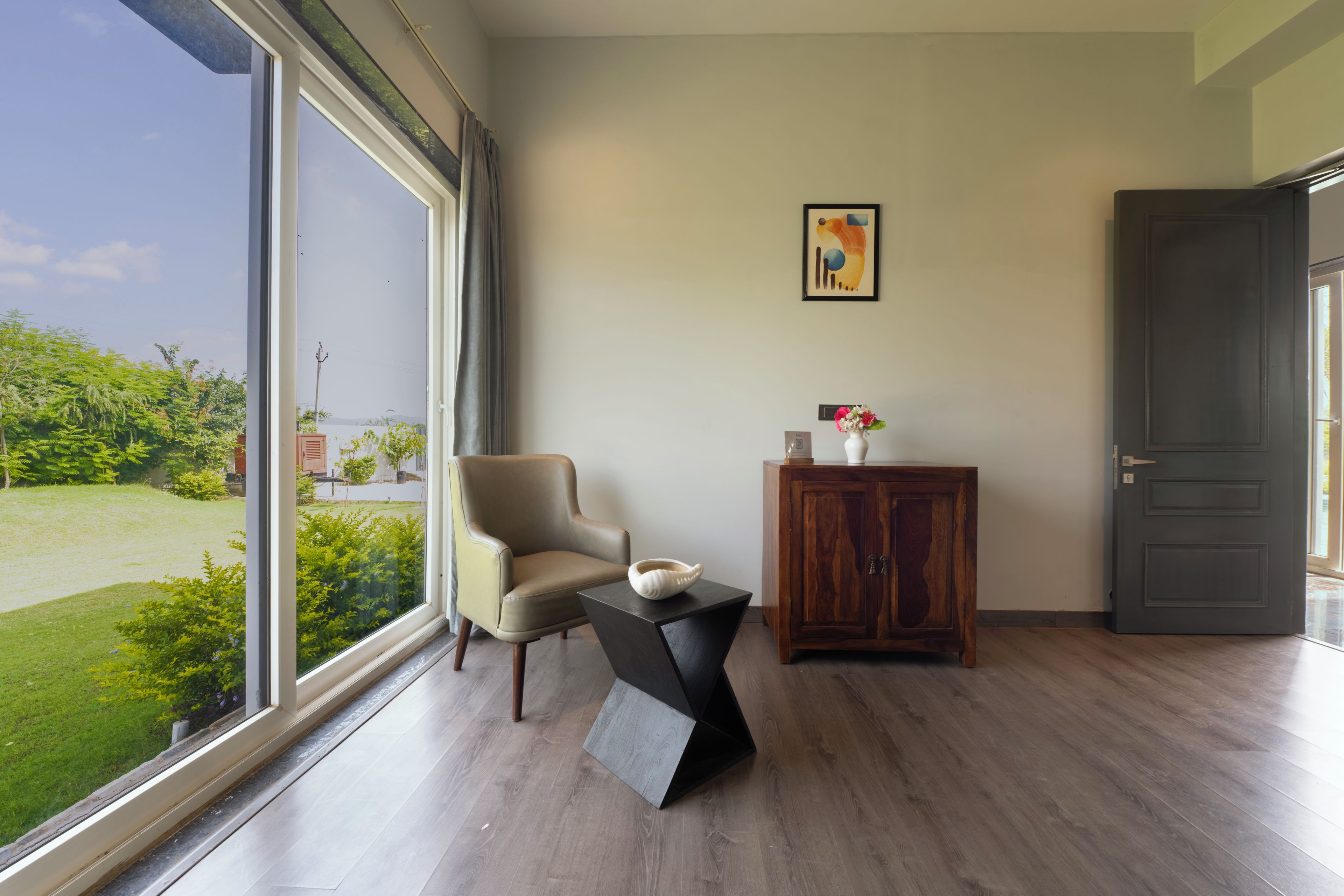 A room with a large window, a chair, a small table with a bowl, a cabinet, and a door.