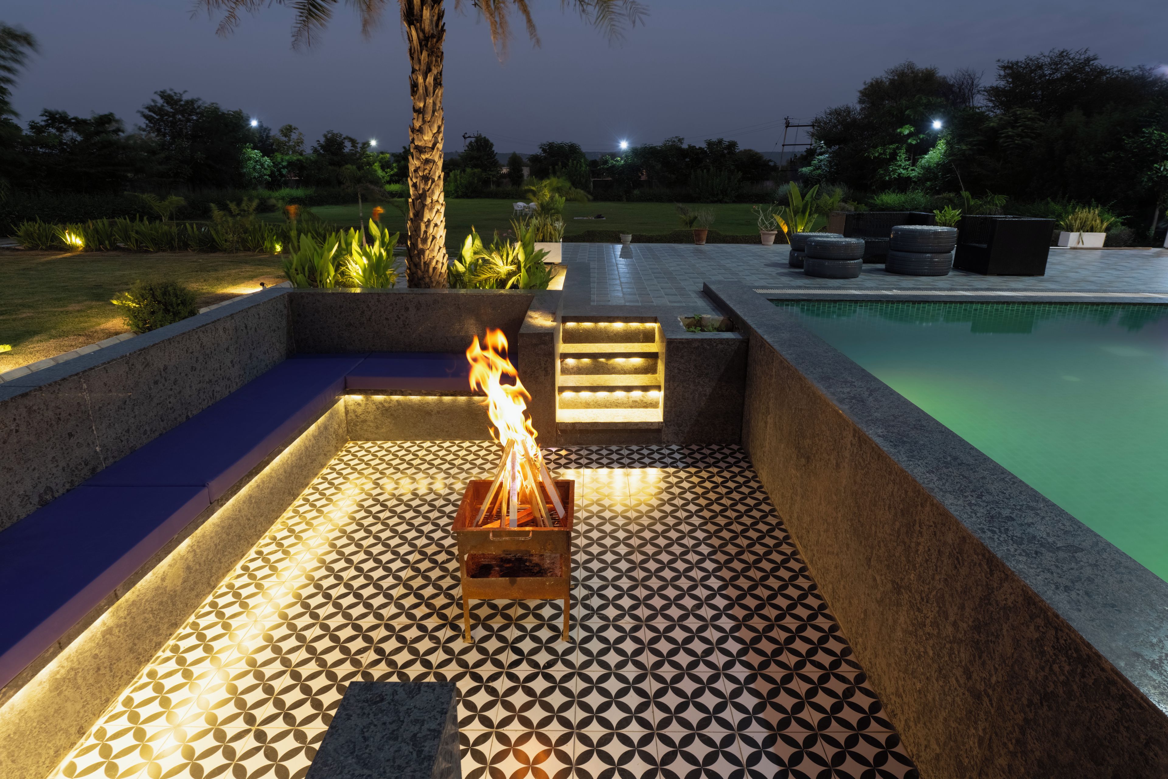A poolside area with a fire feature, seating, and a tiled floor.
