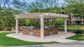 An outdoor grill area with a pergola, stone counter, and a small pond in the background. - Worldmark Indio (Indio)