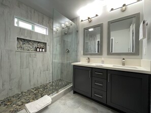 Un baño moderno con cabina de ducha acristalada, paredes de mármol y tocador con un espejo grande.