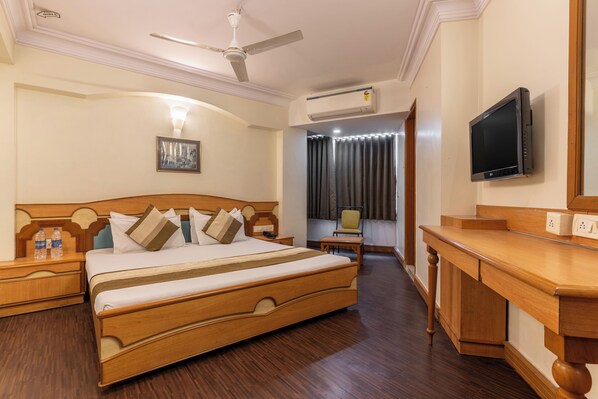 A hotel room with a wooden bed, a desk, a television, and an air conditioning unit.