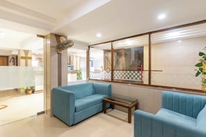 A reception area with a reception desk, a blue sofa, a small table, and a decorative wall with a clock and a checkered pattern. - Hotel Prime (Ahmedabad)