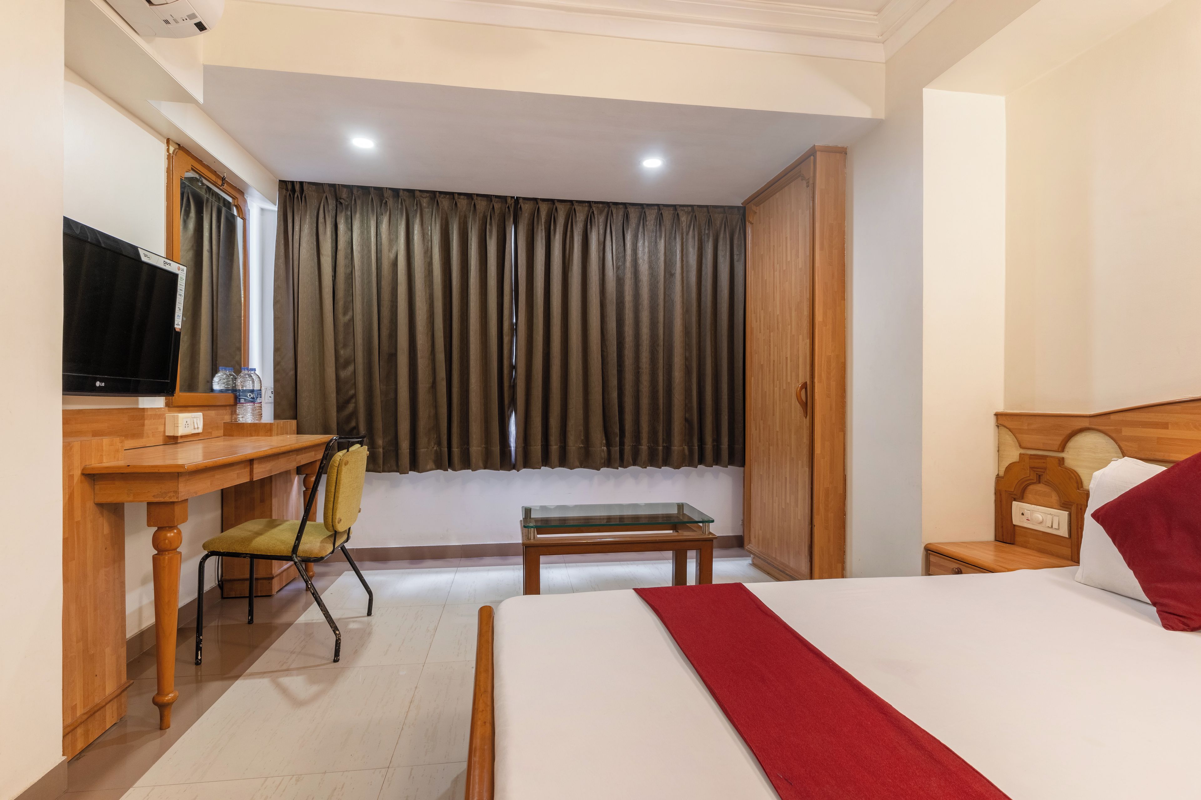 A hotel room with a bed, a desk with a chair, a television, and a window with curtains.