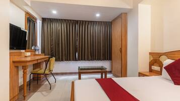 A hotel room with a bed, a desk with a chair, a television, and a window with curtains.