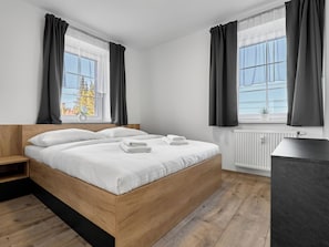 A modern bedroom with a wooden bed, white bedding, and a view of the outdoors through large windows. - George 05 by Interhome (Kovářská)