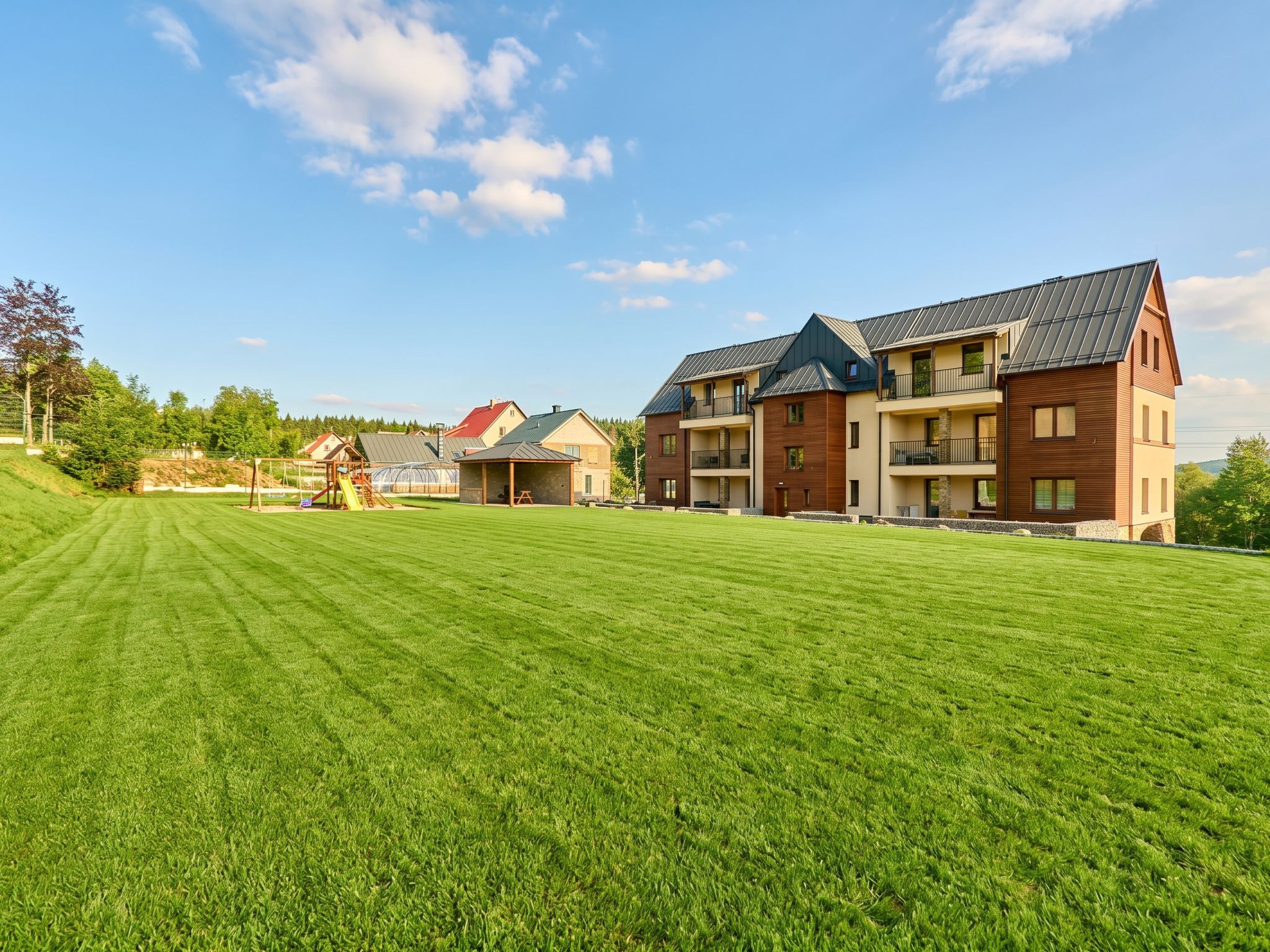 A residential area with a large green lawn, a playground, and multi-story houses with balconies.