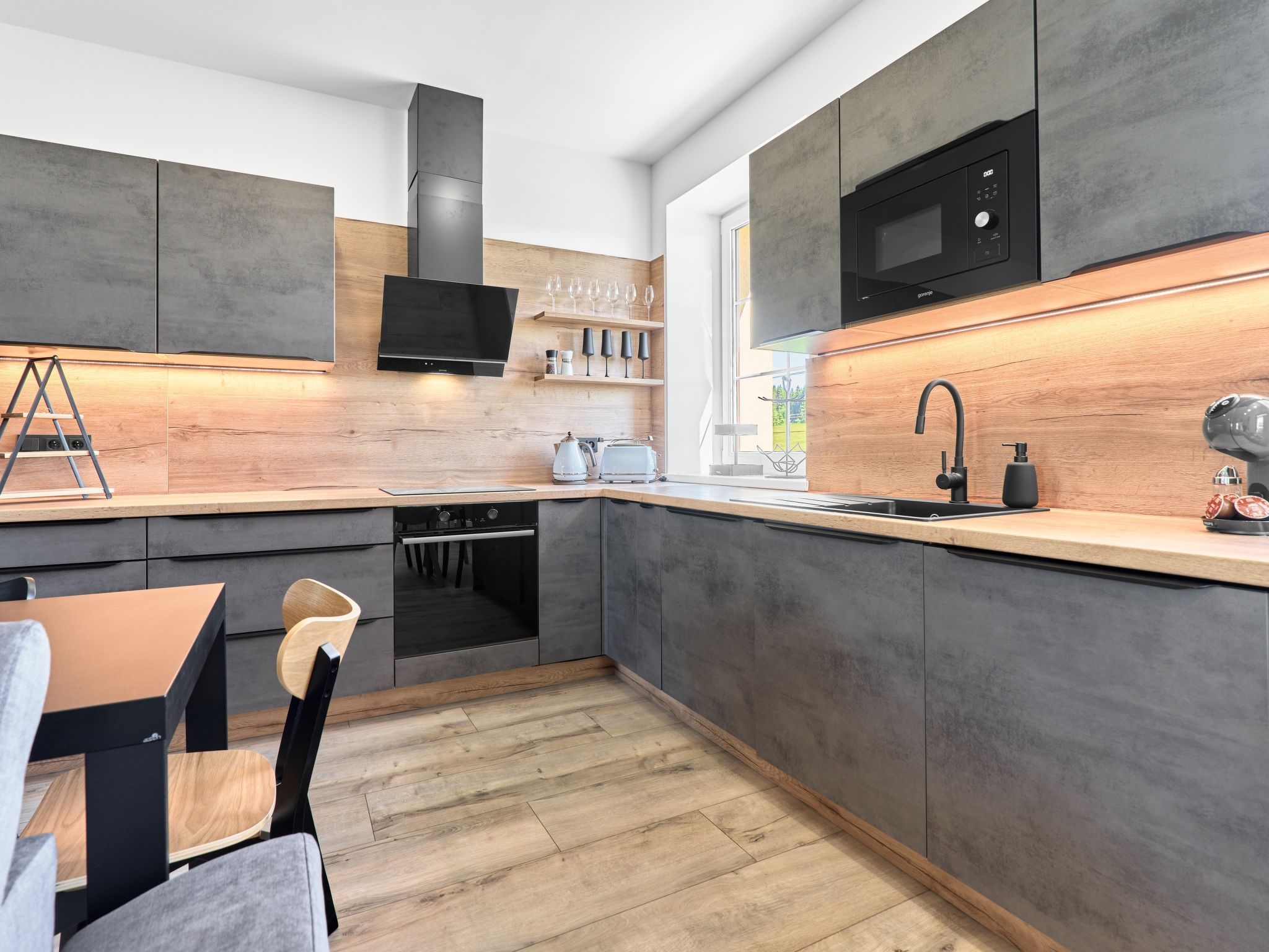 Una cucina moderna con mobili grigi, un forno a microonde nero e un piano di lavoro in legno.