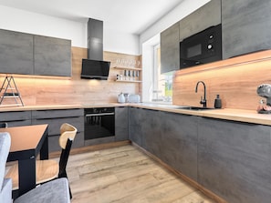 A modern kitchen with grey cabinetry, a black microwave, and a wooden countertop. - George 03 by Interhome (Kovářská)