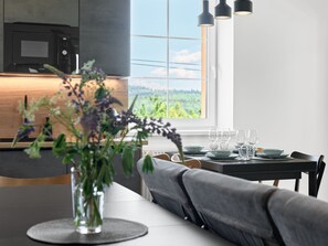 A modern kitchen with a built-in microwave, a dining area with a table set for four, and a large window offering a view of greenery.