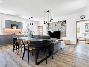 A modern kitchen with a dining area, a flat-screen TV, and a large abstract painting on the wall. - George 03 by Interhome (Kovářská)