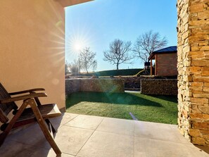 Eine Terrasse mit Steinmauer, einer Holzbank und Blick auf einen Spielplatz und Bäume.