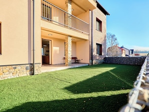 Ein modernes, zweistöckiges Haus mit Naturstein-Fassade, einem Balkon und einem gepflegten Rasen.