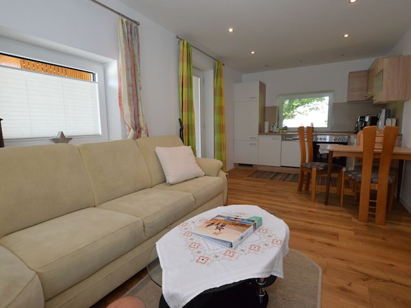 Een woonkamer met een bank, een salontafel met een boek, een keuken met een eettafel en stoelen, en een raam met gordijnen.