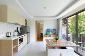 A modern kitchen with a dining area, a TV, and a balcony with a view. - Kamala Fantasia 2-bdr Apartment by TVC (Tambon Kamala)
