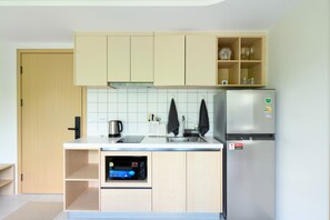 A modern kitchen with light wood cabinets, a stainless steel refrigerator, a built-in oven, and a coffee maker. - Kamala Fantasia 2-bdr Apartment by TVC (Tambon Kamala)