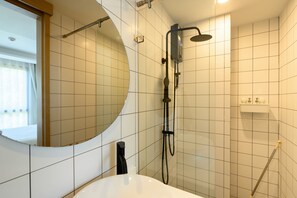 Ein Badezimmer mit einer weißen Badewanne, einem runden Spiegel und einer Dusche inklusive Duschbrause.