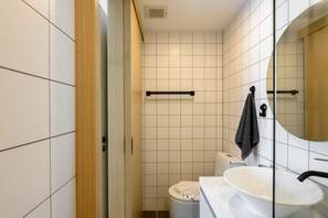 A modern bathroom with white tiles, a white sink, and a mirror. - Kamala Fantasia 2-bdr Apartment by TVC (Tambon Kamala)