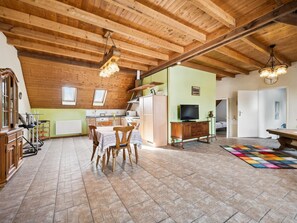 A spacious living area with a high wooden ceiling, a dining table with chairs, a television, and a kitchen area with a refrigerator and microwave. - Apartment with a rooftop terrace on a horse farm (Jüchen)