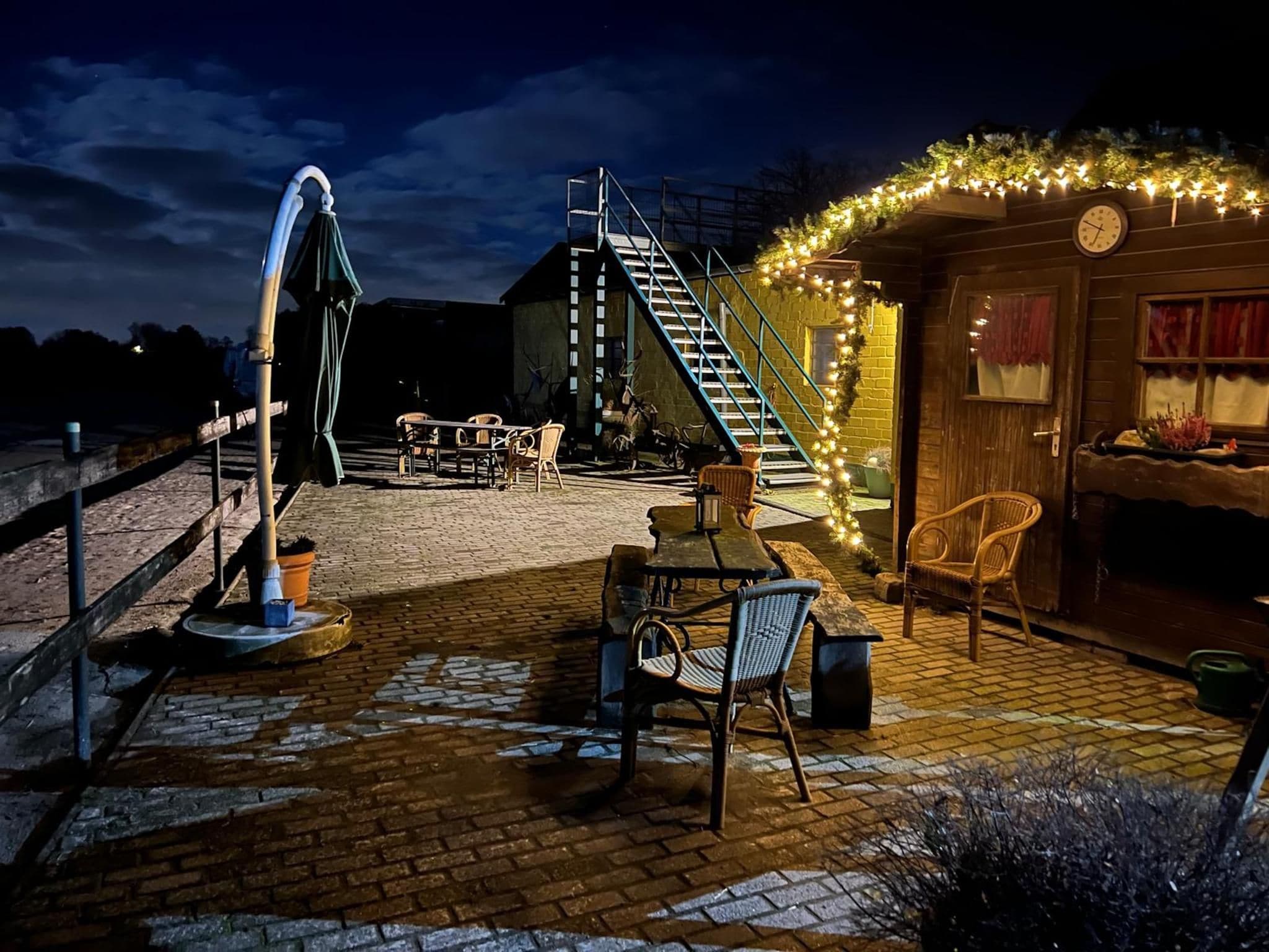 Une terrasse en briques avec des sièges extérieurs, un escalier et un bâtiment décoré de guirlandes lumineuses.