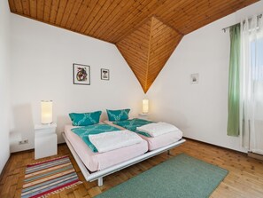 Une chambre avec un plafond en bois, deux lits avec une literie turquoise et blanche, un tapis rayé aux couleurs vives et un tapis vert sur le sol.