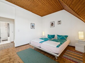 A bedroom with a sloped ceiling, a bed with teal and white bedding, two wall-mounted lamps, and a small rug on the floor. - Apartment with a rooftop terrace on a horse farm (Jüchen)