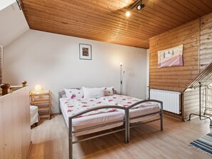Un dormitorio con techo de madera, una cama con ropa de cama floral, una mesita de noche con lámpara y un radiador.