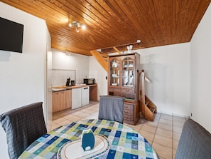 Een knus vertrek met een houten plafond, een eettafel met een quilt, een kast met glazen deuren en een keukenhoek met een magnetron.