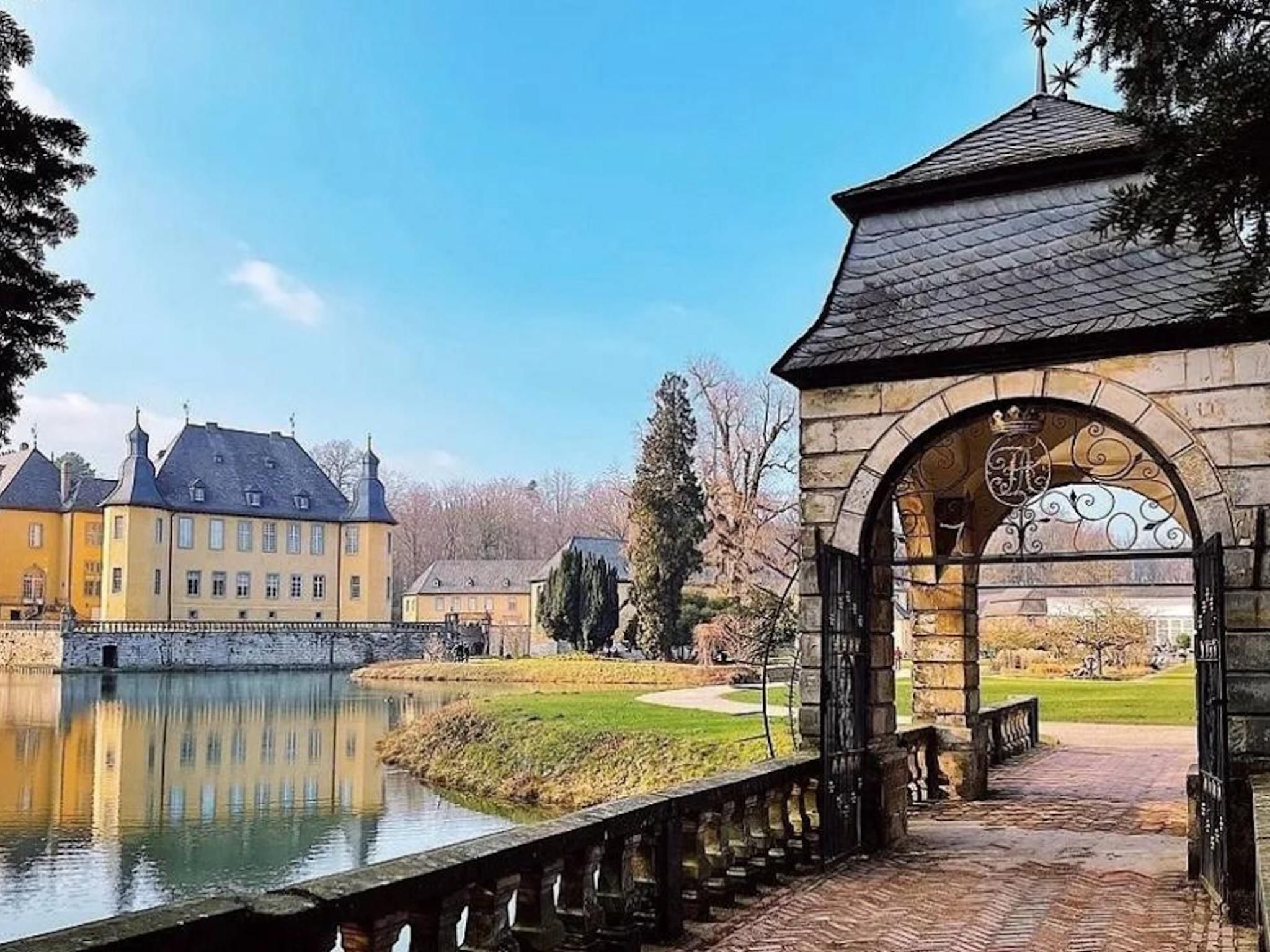 Un bâtiment historique, avec un plan d’eau devant, un pont de pierre et un ciel dégagé.