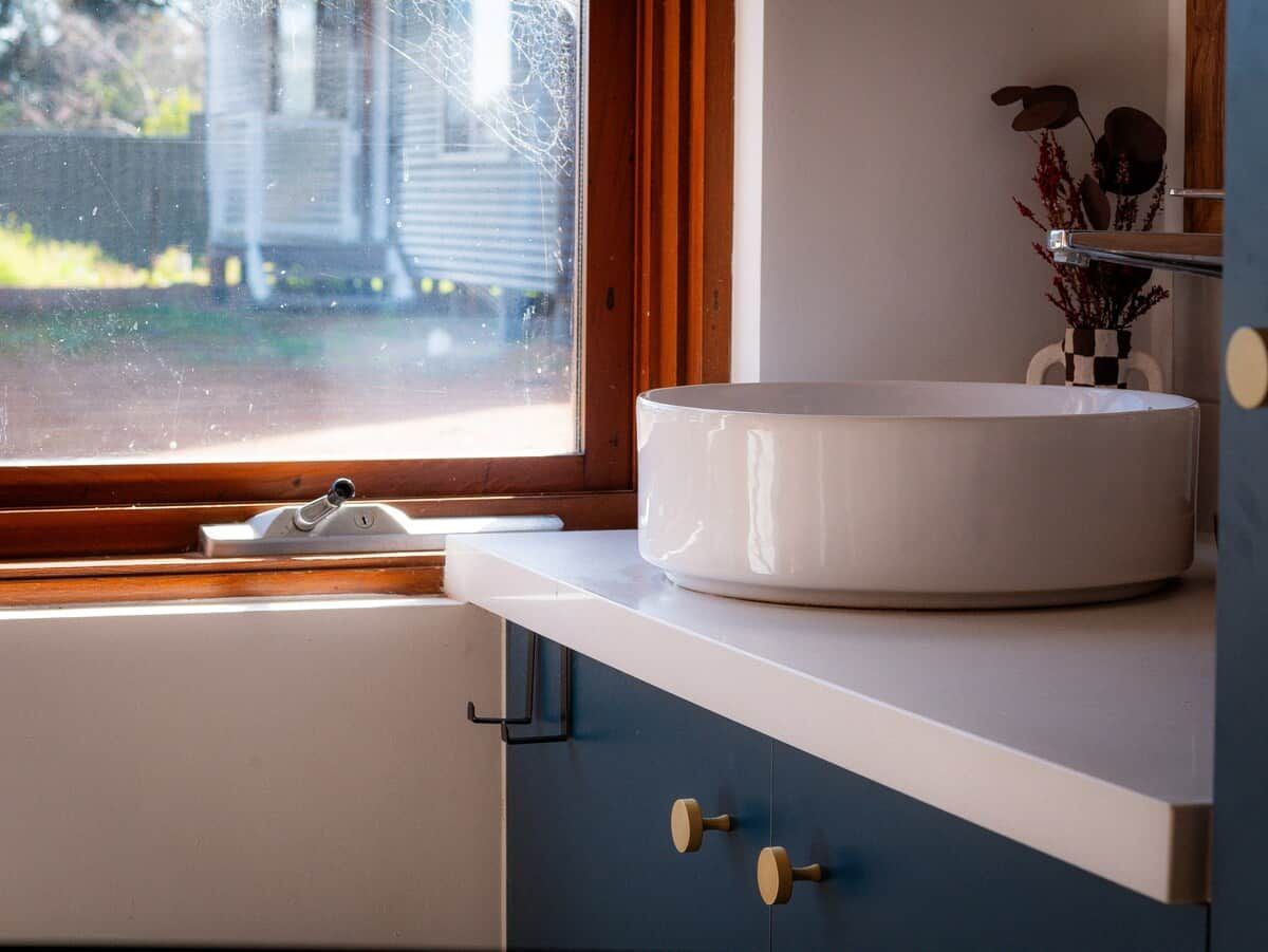 A bathroom with a round white sink, a window with a view of a house, and a cabinet with a towel rack.