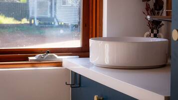 A bathroom with a round white sink, a window with a view of a house, and a cabinet with a towel rack.