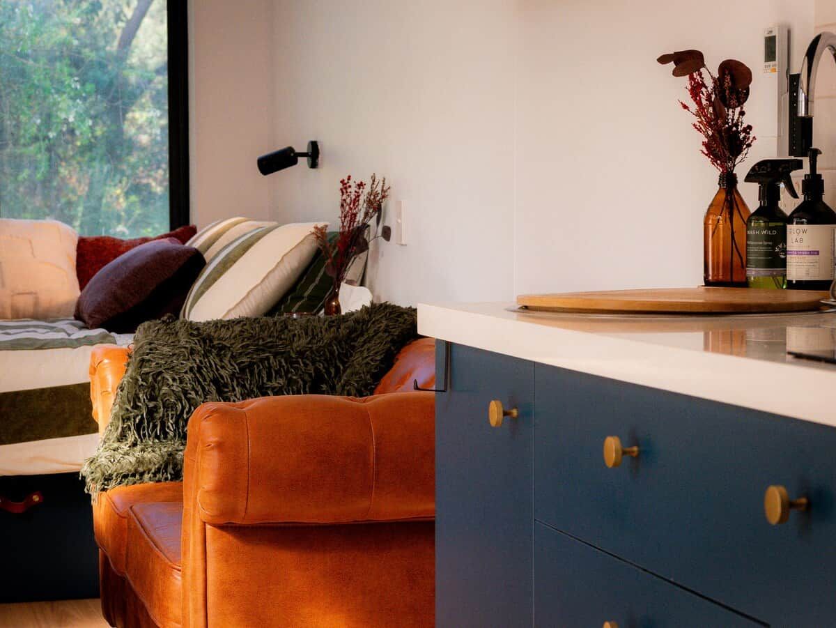 A modern living room with a sofa, a small table, and a kitchen area with cabinets and a sink.