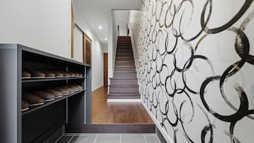 Un pasillo con un zapatero, una escalera y un papel tapiz estampado.