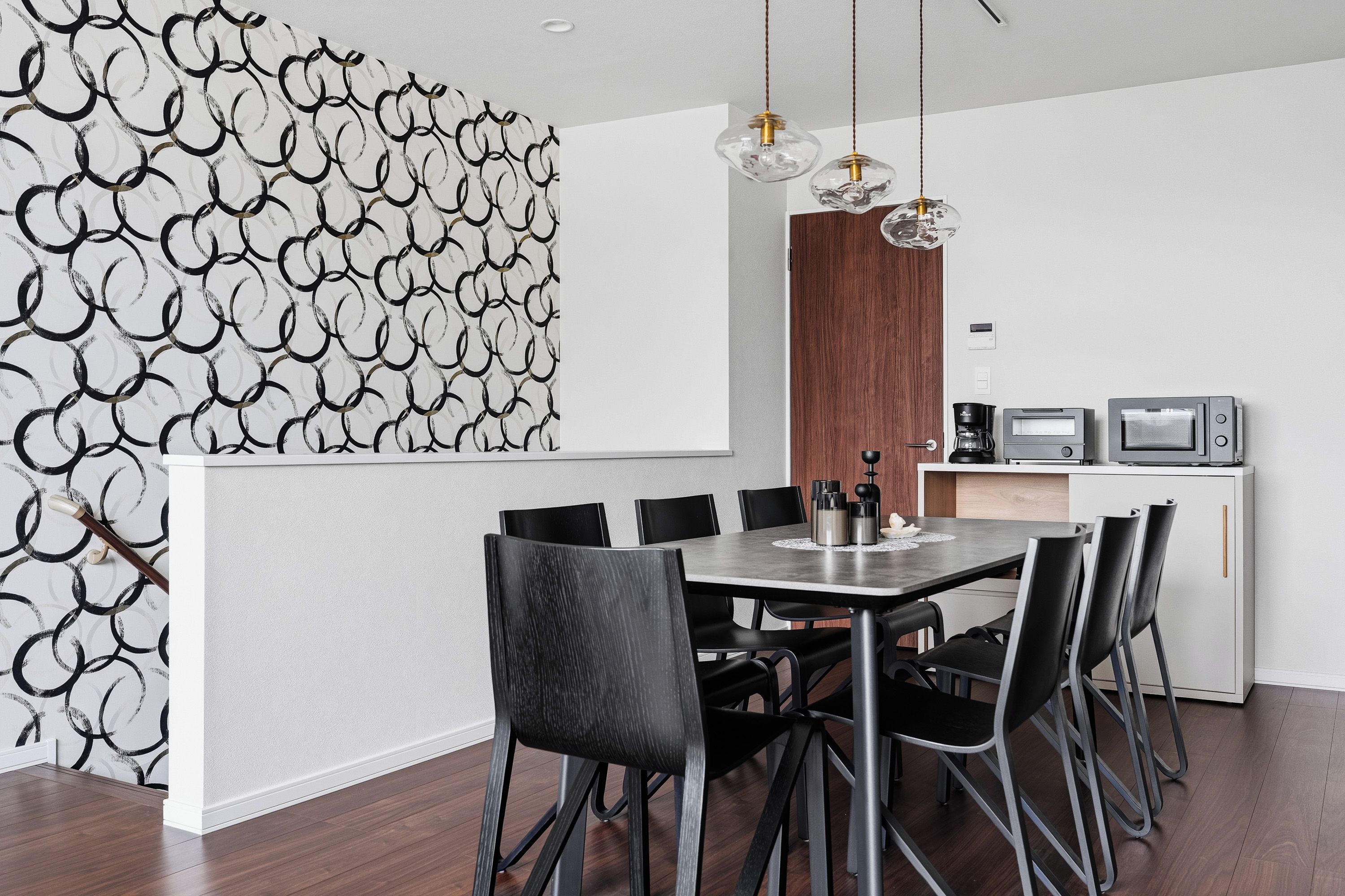 A modern dining area with a round table, black chairs, and a kitchen area with appliances.