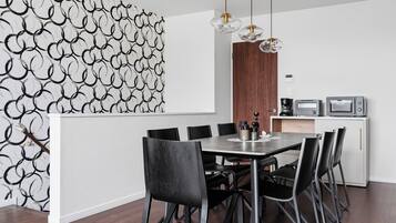 A modern dining area with a round table, black chairs, and a kitchen area with appliances.