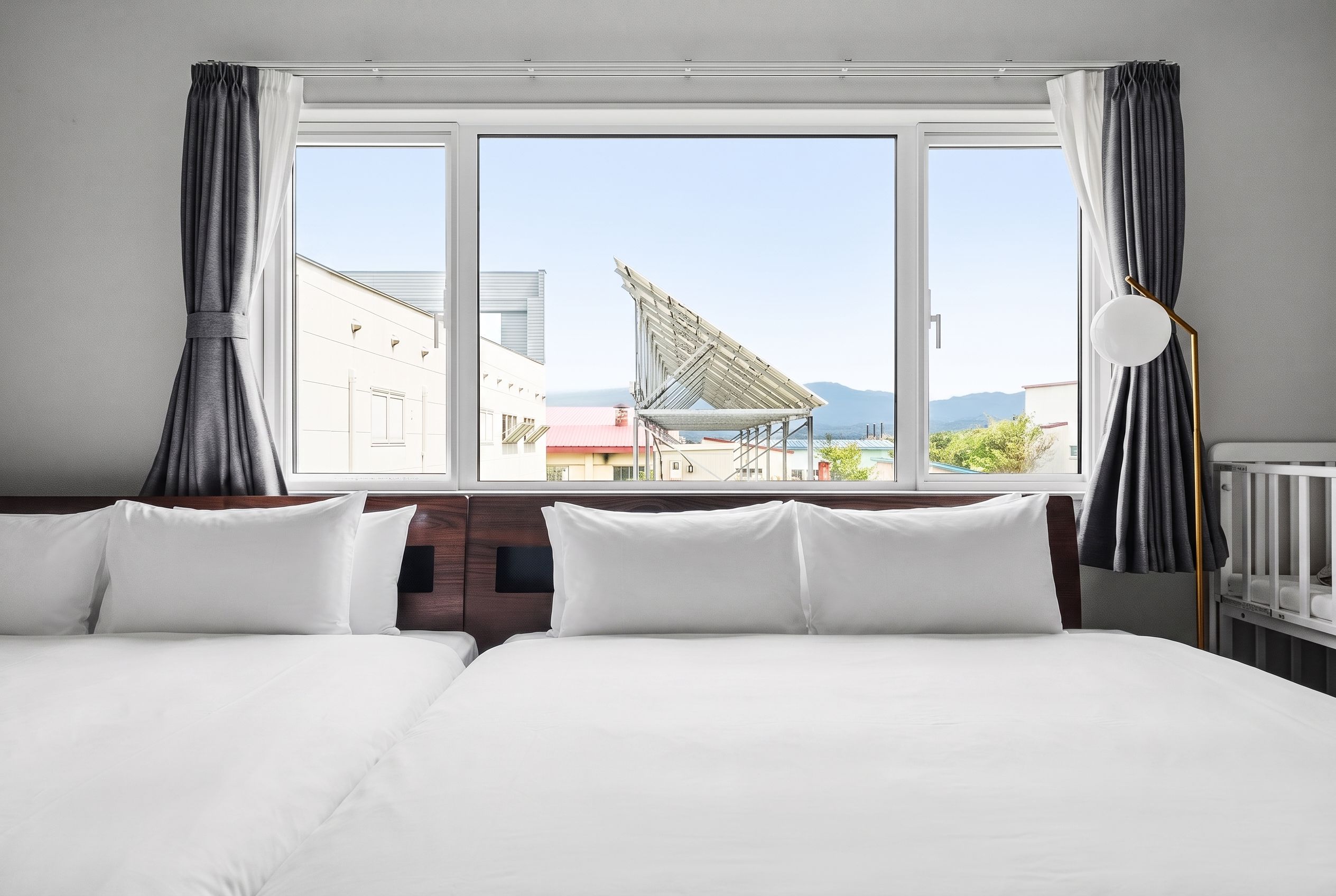 A hotel room with a large bed, a view of buildings and mountains, and a satellite dish.