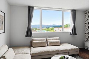 A modern living room with a beige sofa, a small coffee table, and a window with curtains. - Flower (Furano)