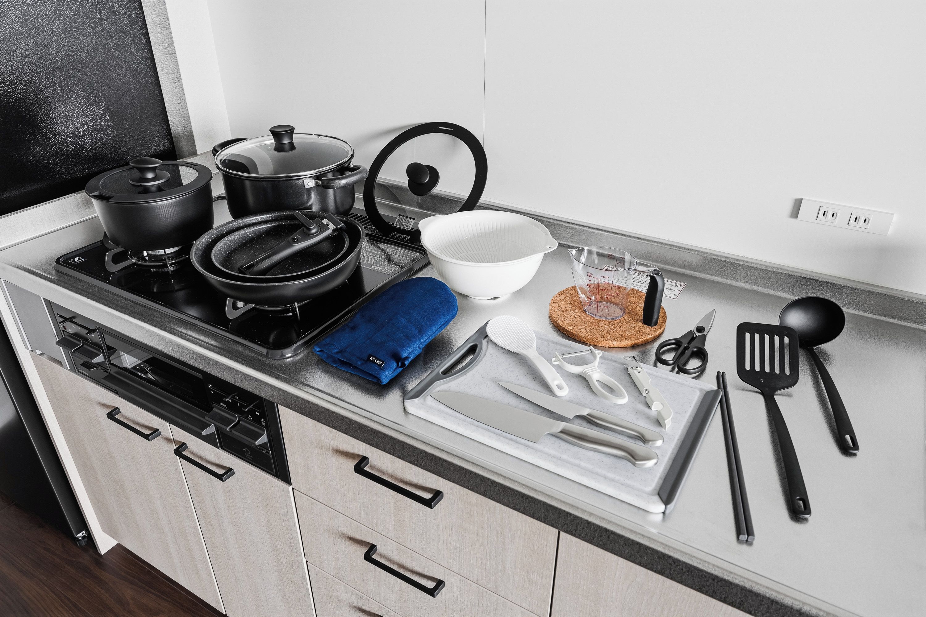A kitchen with a stove, pots, a cutting board, a bowl, a measuring cup, and various utensils.