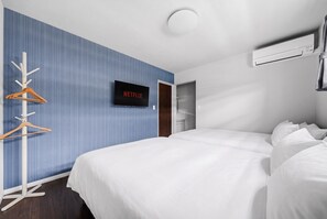 Habitación de hotel con cama, televisión montada en la pared, perchero y aire acondicionado.