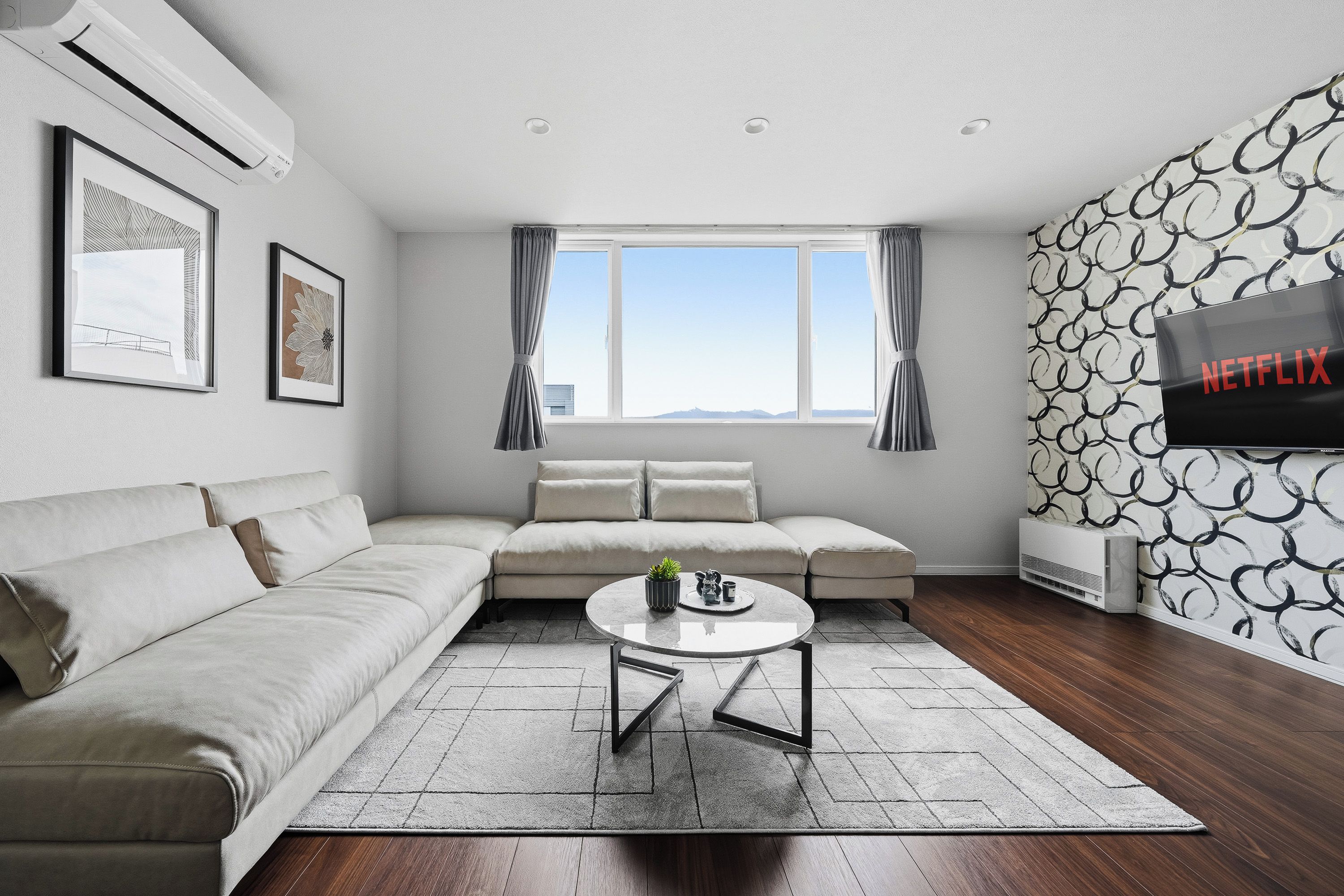 A modern living room with a sectional sofa, a coffee table, a flat-screen TV, and a patterned wall.