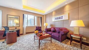 A hotel room with a sofa, armchairs, a desk, a lamp, a mirror, and a patterned carpet.