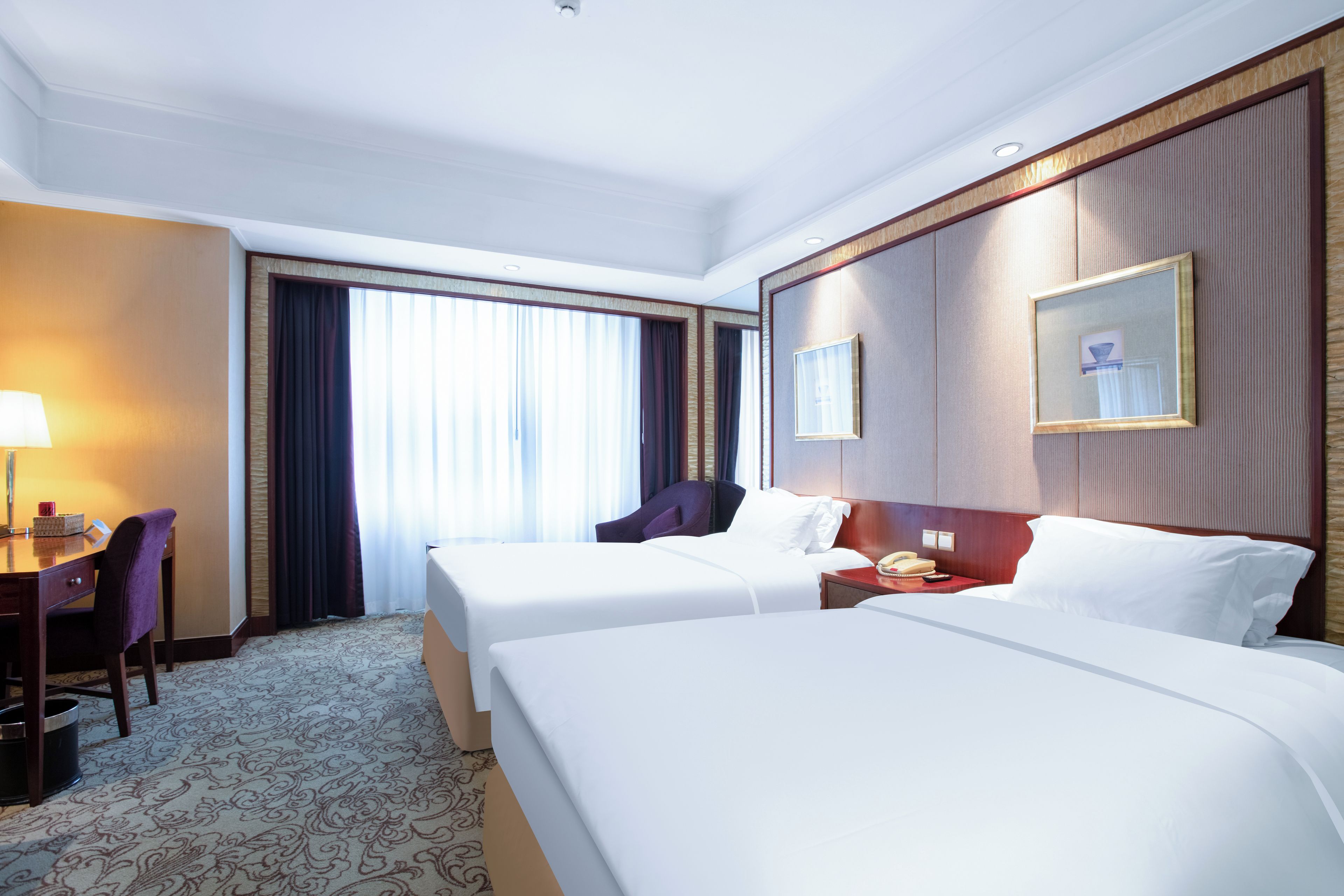 Habitación de hotel con dos camas, un escritorio, una silla, un teléfono y una ventana con cortinas.