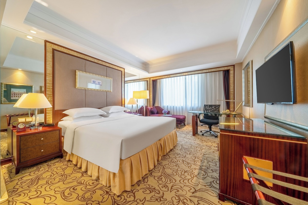 Una habitación de hotel con una cama grande, un escritorio, una silla, un televisor y una ventana con cortinas.