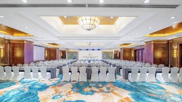 A conference room with rows of tables and chairs, a large chandelier, and a patterned carpet.