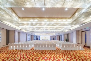 Un salón de conferencias con filas de sillas blancas, una alfombra estampada y un techo con un aplique decorativo.