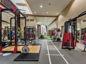 Un gimnasio con diversos equipos de ejercicio, un muro con espejos y vistas a un paisaje urbano.