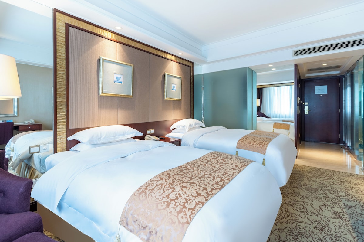 Habitación de hotel con dos camas, un espejo grande y vista al pasillo.