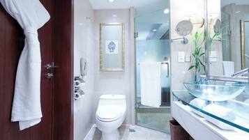 A modern bathroom with a glass sink, a toilet, and a shower area.